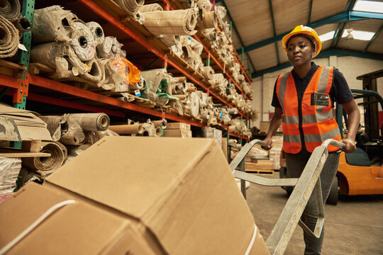 African female warehouse worker moving stock using a dolly
