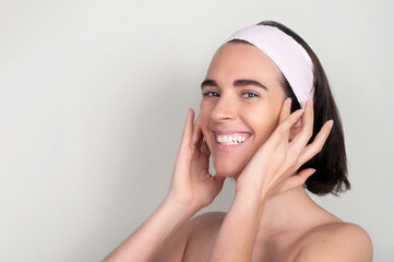 Happy young woman with headband standing and touching face with fingers