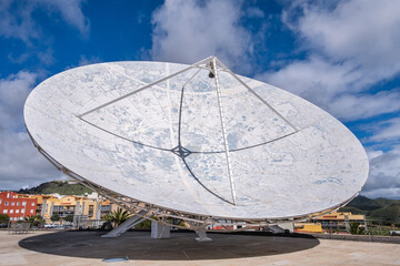 View of a large satellite dish to observe the cosmos, decorated with the lunar topography, with large white clouds in the background.