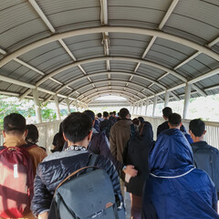 Crowd of people walking on pedestrian bridge to bus shelter at Palmerah train station in morning.