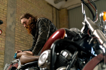 Creative authentic motorcycle workshop Garage of red bearded biker mechanic wiping beautiful...