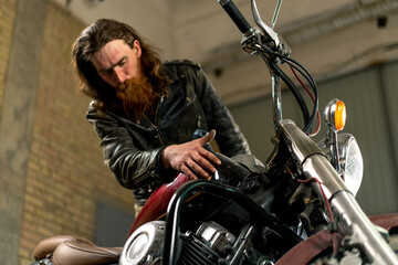 Creative authentic motorcycle workshop Garage of red bearded biker mechanic wiping beautiful motorcycle with rag