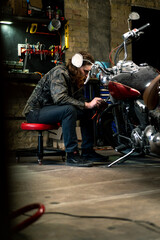 Fototapeta na wymiar Creative authentic motorcycle workshop Garage redhead bearded biker mechanic is concentrating on repairing motorcycle