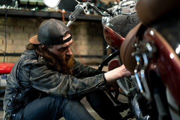 Fototapeta na wymiar Creative authentic motorcycle workshop Garage redhead bearded biker mechanic is concentrating on repairing motorcycle