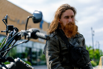 brutal thoughtful redhead bearded biker sitting on a black motorcycle after a race lust for speed...