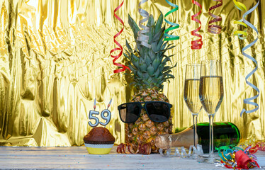 Cheerful pineapple in glasses festive happy birthday character with number  59. Beautiful background for congratulations copy space on a golden background with glasses of champagne. Anniversary