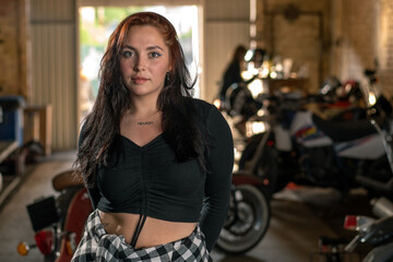 Plakat Creative authentic motorcycle workshop garage beautiful young biker girl standing near a cool motorcycle