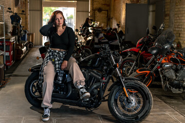 Creative authentic motorcycle workshop garage beautiful young girl biker sitting on a cool...