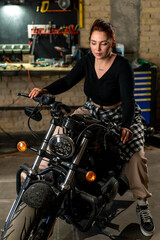 Naklejka na ściany i meble Creative authentic motorcycle workshop garage beautiful young girl biker sitting on a cool motorcycle