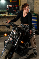 Obraz na płótnie Canvas Creative authentic motorcycle workshop garage beautiful young girl biker sitting on a cool motorcycle