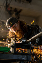 Creative authentic motorcycle workshop redhead bearded brutal biker works with circular saw Sparks fly from hot metal