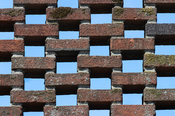 brick wall of open lattice bricklaying pattern with the blue sky peering though the spaces in the brickwork make a unique background, moss grows on some bricks