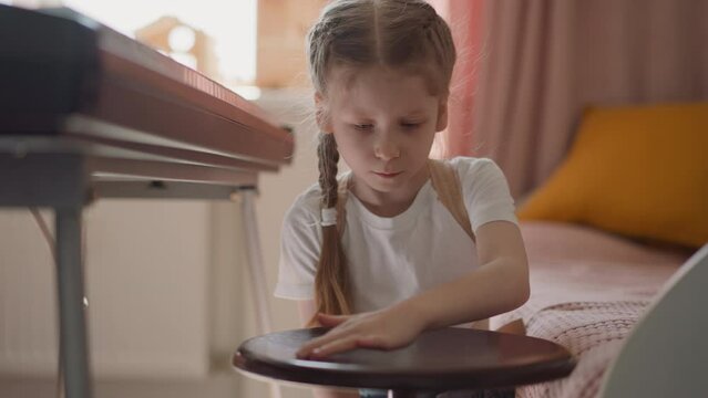 Girl in t-shirt plays with stool by electric piano at home
