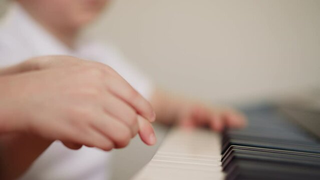 Little girl plays piano music with toddler boy index finger on blurry background closeup. Elder sister learns composition with brother on musical instrument