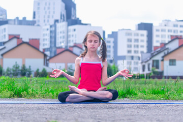 Fototapeta na wymiar Young girl sitting in yoga lotus pose against city background as symbol of maintaining peace of mind and balance, common sense in the conditions of the super-fast pace of the city