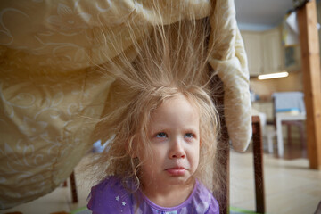 Sad girl is sitting at home with electrified hair sticking up. Children's games for preschoolers at...