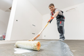 Closeup floor priming process. Worker use primer on concrete floor before leveling, strengthening...