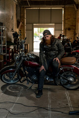 Creative authentic motorcycle workshop Garage brutal serious bearded biker mechanic sitting on motorcycle