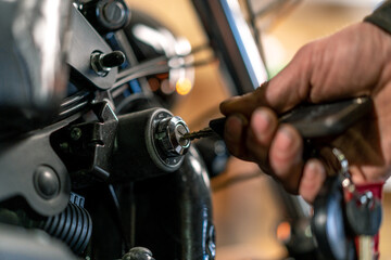 Fototapeta na wymiar Creative authentic motorcycle workshop Biker mechanic in garage putting key into power box to start motorcycle close up