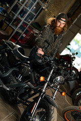 Fototapeta na wymiar Creative authentic motorcycle workshop Garage redhead bearded biker mechanic standing near motorcycle checking it