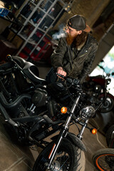 Fototapeta na wymiar Creative authentic motorcycle workshop Garage redhead bearded biker mechanic smoking cigarette near motorcycle