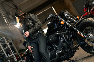 Creative authentic motorcycle workshop Garage redhead bearded biker mechanic smoking cigarette near...