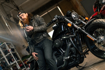 Plakat Creative authentic motorcycle workshop Garage redhead bearded biker mechanic smoking cigarette near motorcycle