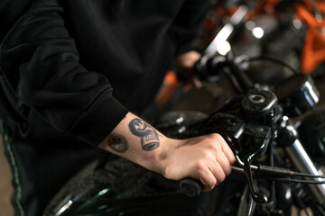 close-up of hand of tattooed biker holding motorcycle handlebar in workshop garage checking gas knob