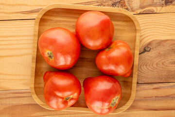 Several red tomatoes with bamboo tray on wooden table, macro, top view.