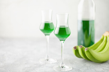 Green banana liqueur in grappas glasses and fresh  bananas on the table. Copy space
