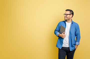 Happy male freelancer with hand in pocket holding digital tablet looking away over yellow background - obrazy, fototapety, plakaty