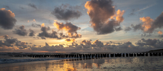 Sunset with colorful sky and clouds and wooden posts at Westenschouwen, Zeeland, the Netherlands