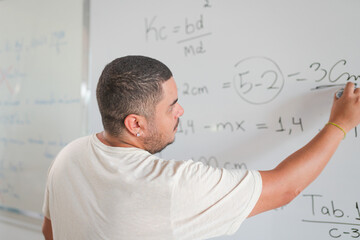 Brazilian teacher explaining a math problem on the blackboard during class in an adult course in...
