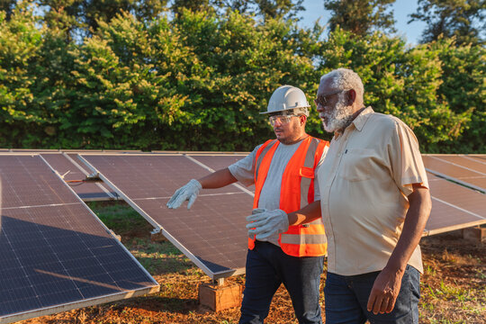 técnico de instalação de painéis fotovoltaicos vestindo equipamentos de segurança explicando sobre a energia solar para o fazendeiro Brasileiro