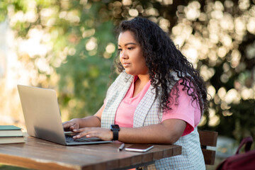 Young woman with laptop studying online outdoors sitting with books