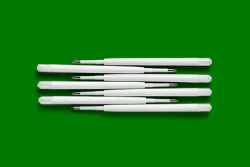 Ballpoint pen refills. Plastic refills for ballpoint pens. Stack of white ink refills on a green