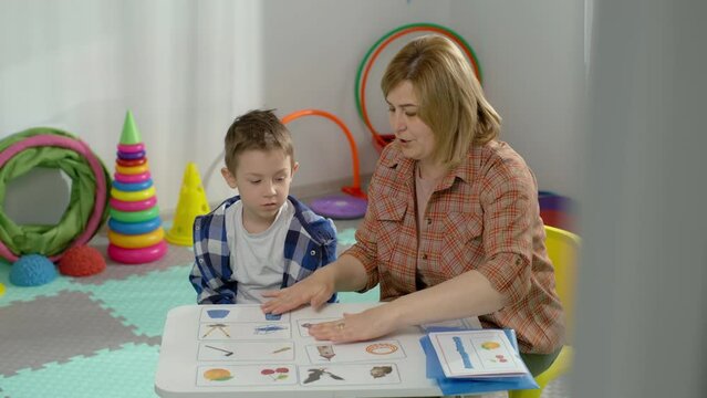 The teacher shows the child how to correctly perform tasks with pictures. Learning and developing games at school. The boy studies at the desk in the classroom. High quality 4k footage