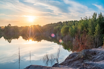 Fototapeta premium Beautiful landscape with colorful sunset over forest lake, Epic red and golden clouds above the forest lake at sunrise. Dramatic cloudscape. Symmetry reflections on the water, natural mirror. Idyllic