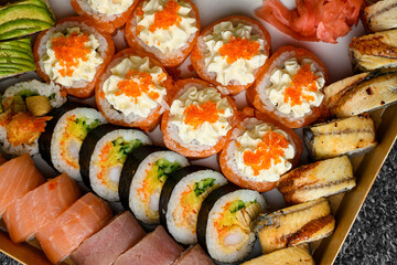 Mix of sushi rolls with salmon, avocado, smocked eel, tobiko caviar in delivery box on black background