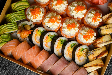 Set of sushi rolls with salmon, avocado, smocked eel, tobiko caviar in transport box on black background