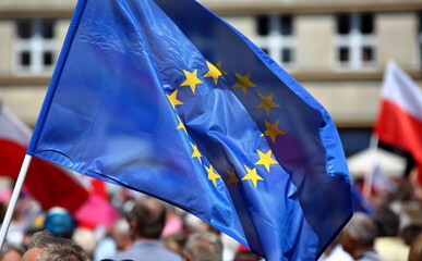 European union flag waves on street demonstration, protesters with flags of Poland in background