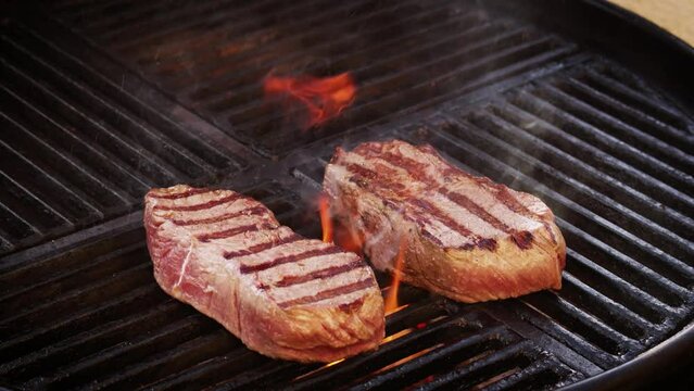Barbecue dry aged roast beef steaks grilled as close-up on a charcoal grill with fire and smoke  &ndash; video 