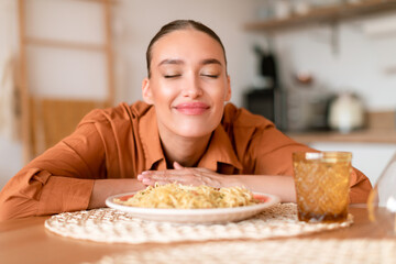Italian cuisine. Happy satisfied european woman smelling fresh spaghetti on plate, enjoying tasty...