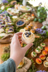 Female guest at rustic outdoor party holding mini Pavlova dessert with fresh blueberries