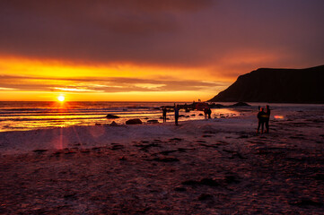 Sunset into the sea on a sandy beach with silhouettes of people - Skagen, Lofoten, Norway.