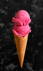 Pink ice cream two balls in a waffle cone on a dark background