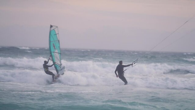 A wind surfer and a kite surfer surfing on the ocean together at susnet