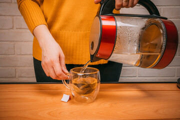 woman pouring hot water from a kettle into a clear glass mug