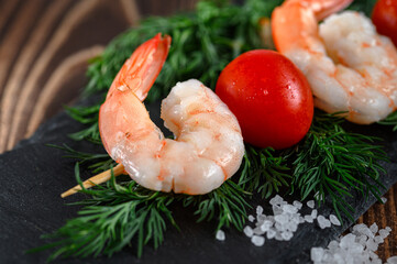 Peeled shrimps and red tomato on a wooden stick and dill on stone cutting board