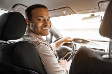 Smiling indian guy driver sitting inside brand new car